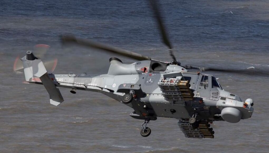 Martlet image Grey military helicopter in flight over water, with rockets mounted on its side and rotor blur indicating motion.