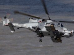 Britain’s Martlet missile reaches full capability on Wildcat Grey military helicopter in flight over water, with rockets mounted on its side and rotor blur indicating motion.