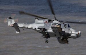 Britain’s Martlet missile reaches full capability on Wildcat Grey military helicopter in flight over water, with rockets mounted on its side and rotor blur indicating motion.