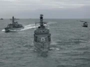 British frigate and helicopter fire torpedo in the Atlantic Three gray military ships sail in formation on the open sea, with a helicopter hovering to the right.