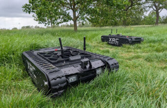 Army awards first fast-tracked UGV contract to UK startup Two black tracked robots with antennas sit in a tall-grass field, one foreground and one in the background, labeled XRC Robotics.