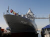 Large gray naval vessel named P6202 docked at a pier, with signal flags along the bow and a gangway extending to shore.