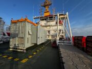NavyPODS passes sea trials but deployment timeline unclear Deck of a large support vessel with a gray containerized generator and an orange crane, against a blue sky and ocean.”