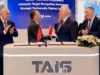 Two men in suits shake hands across a signing desk with Turkish and Georgian flags; colleagues applaud behind a TAIS booth.