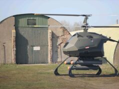 Certo Capstone drone tests Hellfire missile in simulation Futuristic gray helicopter drone with landing skids, labeled Certo Aerospace, parked in a grassy field beside a weathered hangar.