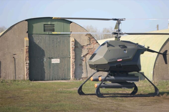 Certo Capstone drone tests Hellfire missile in simulation Futuristic gray helicopter drone with landing skids, labeled Certo Aerospace, parked in a grassy field beside a weathered hangar.