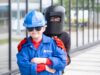 Babcock brings 300 pupils to Rosyth for engineering festival Young child in a blue hard hat and jacket with safety gloves stands in front of a person wearing a welding mask outdoors near a glass building.