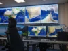 Mission control desk with multiple monitors displaying satellite maps of the Middle East and Indian Ocean; a high-backed chair in front of the setup.