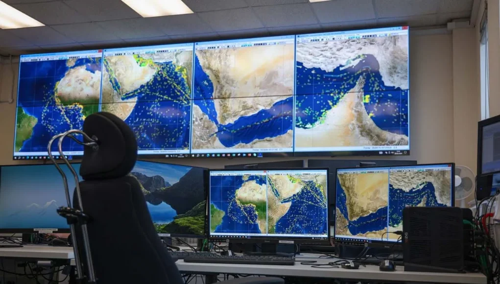 Mission control desk with multiple monitors displaying satellite maps of the Middle East and Indian Ocean; a high-backed chair in front of the setup.