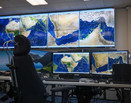 27 nations back Hormuz mission in joint statement Mission control desk with multiple monitors displaying satellite maps of the Middle East and Indian Ocean; a high-backed chair in front of the setup.