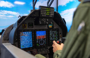 How simulation is speeding up the RAF pilot pipeline Pilot in a cockpit operating flight controls with touchscreen displays and avionics visible ahead of him to the blue sky outside the canopy.