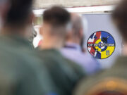 Ukrainian pilots graduate from British flying programme Circular patch reading 'OP INTERSTORM' with blue, red, and yellow segments, seen among blurred soldiers in the foreground.