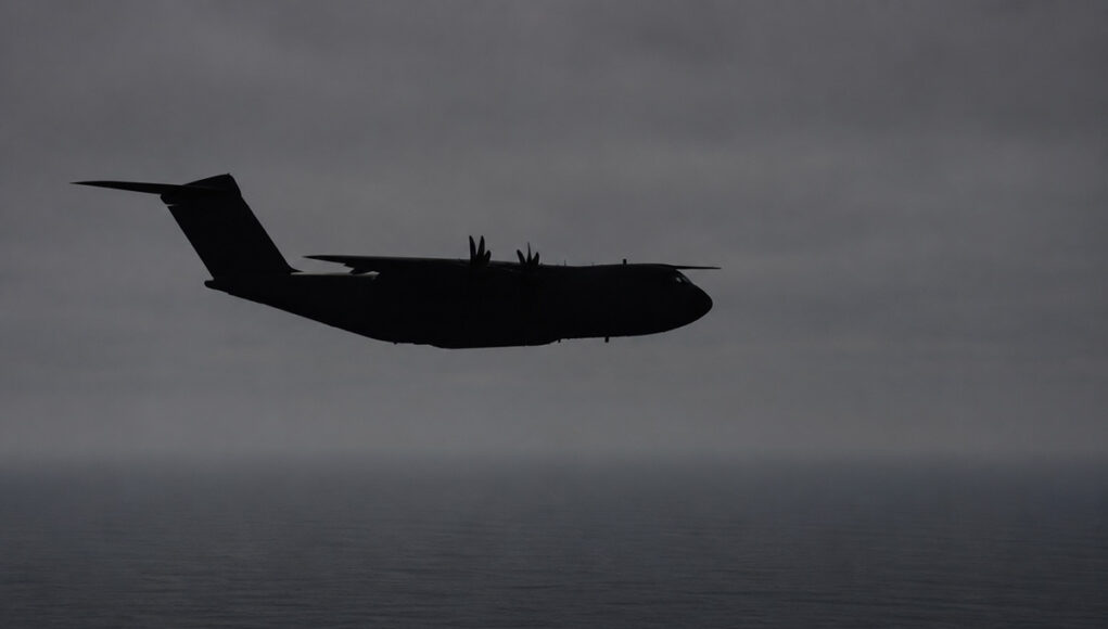 a400mgeneric Silhouette of a four-engine military transport aircraft (C-130-like) flying over the ocean at dusk with a cloudy sky.