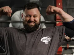 REME soldier first to reach England’s Strongest Man Bearded man in a gym flexing his biceps, wearing an Iron Rhino t-shirt, with weight racks in the background.