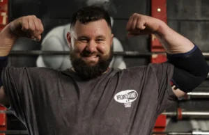 REME soldier first to reach England’s Strongest Man Bearded man in a gym flexing his biceps, wearing an Iron Rhino t-shirt, with weight racks in the background.