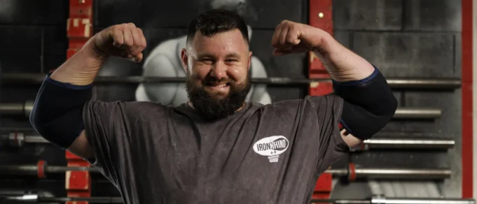 REME soldier first to reach England’s Strongest Man Bearded man in a gym flexing his biceps, wearing an Iron Rhino t-shirt, with weight racks in the background.