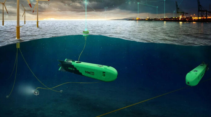 Green autonomous underwater vehicles tethered by cables on a seabed near an offshore wind farm and port at dusk, with the surface showing wind turbines and lights.
