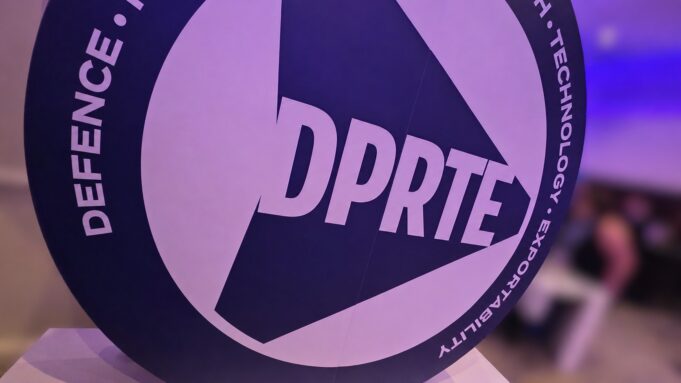 Close-up of a round sign featuring the DPRTE logo at an event or expo setting.