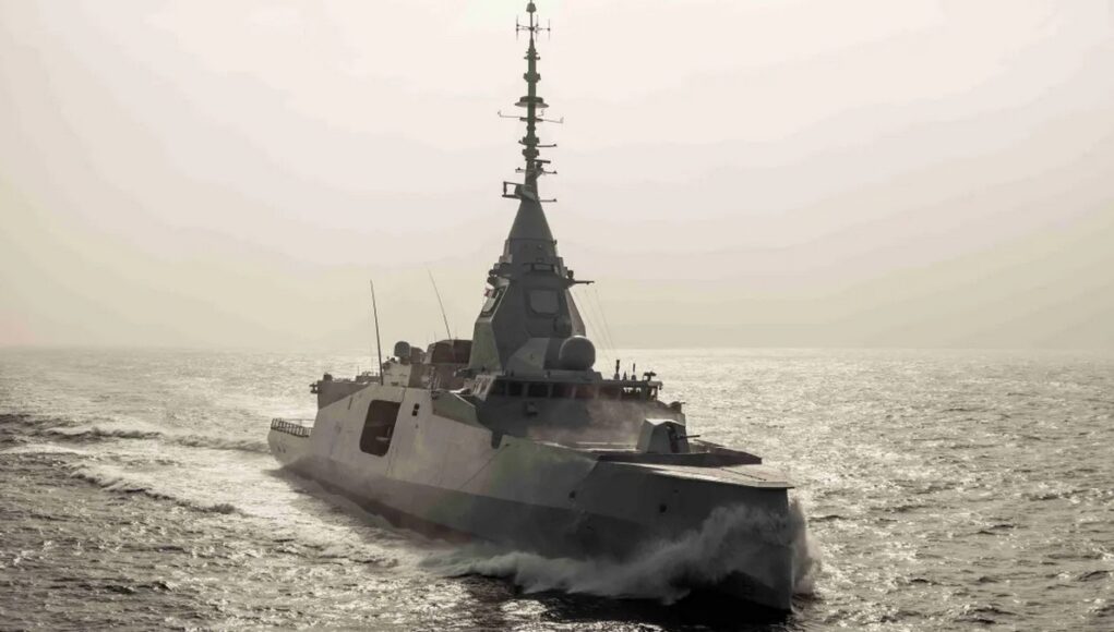 Surface warship sailing on calm sea with wake trailing behind, sun glare on the water.