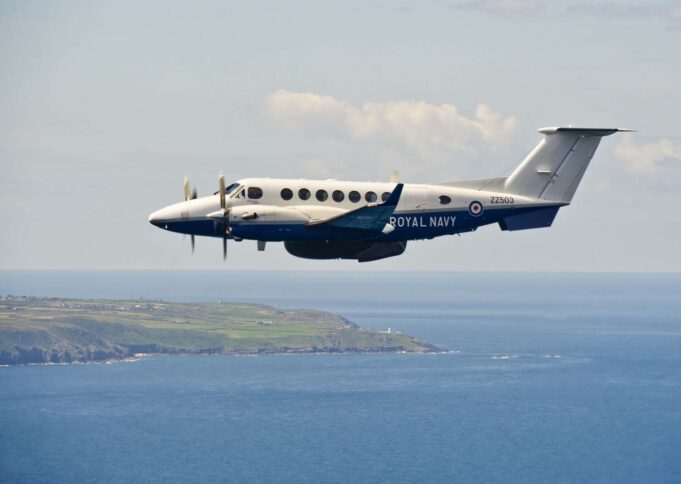 Second upgraded Avenger takes flight at Culdrose Twin-turboprop Royal Navy aircraft (ZZ503) in white and blue livery, flying low over the coastline and sea.