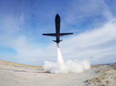 Black jet lifting off from a sandy desert airstrip, exhaust plume blasting upward and creating a cloud at ground level.