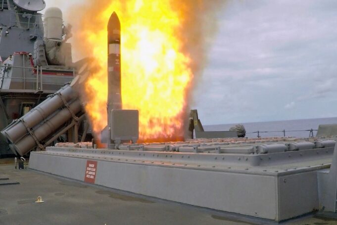 Missile launches from a naval ship's launcher with a large orange flame plume surrounding the rocket.