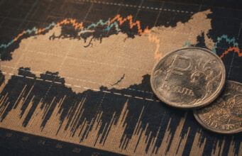 Russia sanctions at a crossroads as US commitment wavers Russian ruble coins placed on a stock market chart showing fluctuating lines and data.