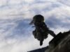 Military paratrooper in camouflage gear free-falling from a aircraft against a cloudy sky.