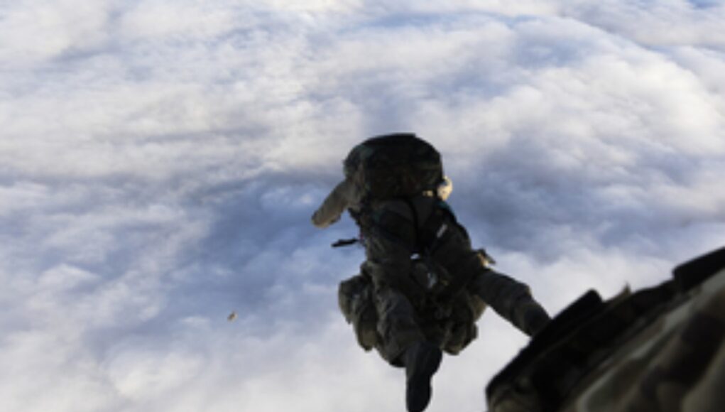 Military paratrooper in camouflage gear free-falling from a aircraft against a cloudy sky.
