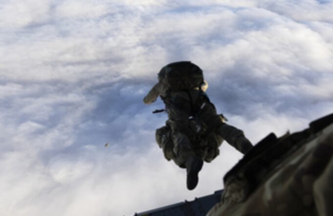 Military paratrooper in camouflage gear free-falling from a aircraft against a cloudy sky.