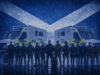 Emergency responders in uniform stand in front of two NHS emergency ambulances with a Scottish flag backdrop behind them.