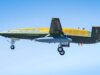 Military aircraft in flight with landing gear down against a clear blue sky, labeled NAVY on its fuselage.