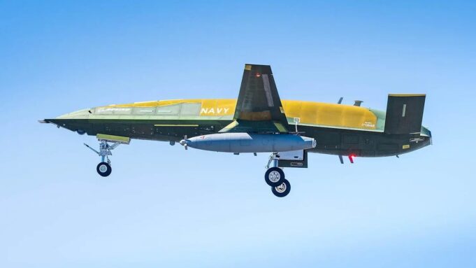 Military aircraft in flight with landing gear down against a clear blue sky, labeled NAVY on its fuselage.