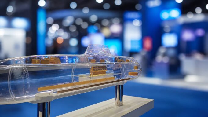 Transparent submarine model on a pedestal, showing orange internal components at a blue-lit expo hall display center.