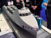 HII showcases REMUS and ROMULUS at CNE Scale model cruise ship on a display table at an exhibition, with people in business attire gathered around.