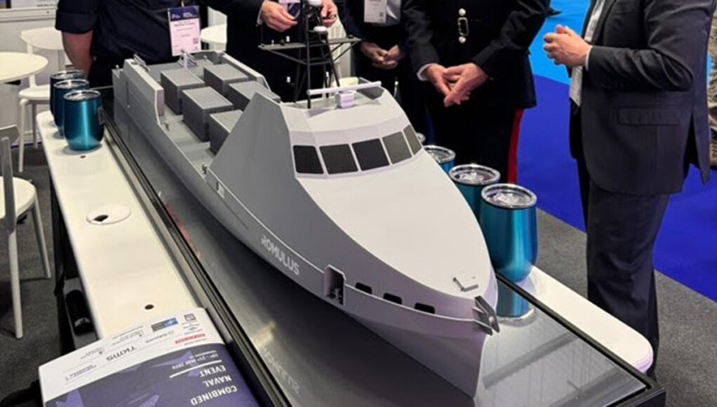 unnamed (15) Scale model cruise ship on a display table at an exhibition, with people in business attire gathered around.