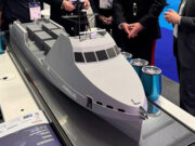 HII showcases REMUS and ROMULUS at CNE Scale model cruise ship on a display table at an exhibition, with people in business attire gathered around.