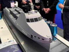 HII showcases REMUS and ROMULUS at CNE Scale model cruise ship on a display table at an exhibition, with people in business attire gathered around.