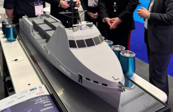 HII showcases REMUS and ROMULUS at CNE Scale model cruise ship on a display table at an exhibition, with people in business attire gathered around.