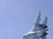 Blurred fighter jet ascending into a clear blue sky, twin vertical tails visible at the rear.