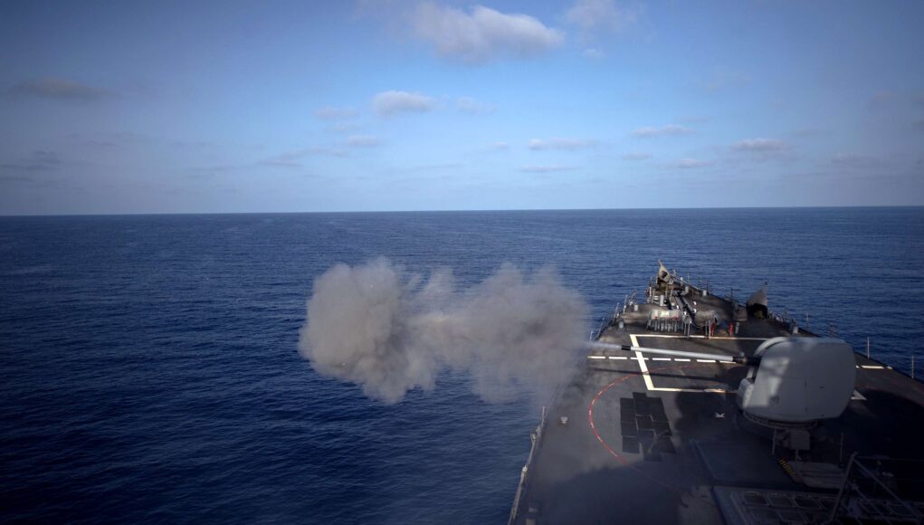 USS Arleigh Burke operations Military ship’s flight/deck at sea with a smoke plume near the bow and open ocean ahead.