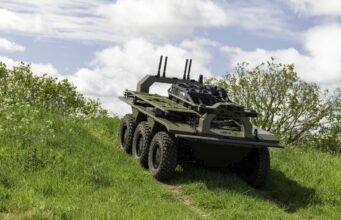 Leonardo deal lets IDV build the Viking UGV at scale Eight-wheeled armored military vehicle on a grassy slope under a cloudy sky, with equipment racks and antennas mounted on top.