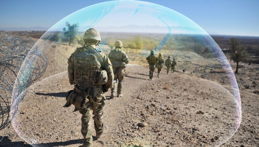Soldiers in camouflage marching along a rocky desert path beside a barbed-wire fence, with a translucent arc overlayed across the scene.