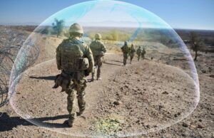 First prototypes of troop-protection jammer due in 2027 Soldiers in camouflage marching along a rocky desert path beside a barbed-wire fence, with a translucent arc overlayed across the scene.
