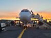 Government rules out fuel shortage behind airport disruption Front view of a passenger airliner at the gate with a jet bridge and sunset in the background, boarding area visible behind it.