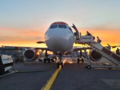 Government rules out fuel shortage behind airport disruption Front view of a passenger airliner at the gate with a jet bridge and sunset in the background, boarding area visible behind it.