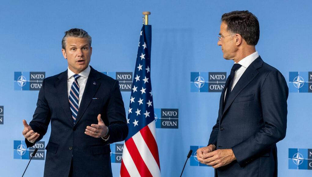 20260618_mod-bilat-us_0017 Two men in dark suits speak at a NATO press conference with the American flag between them.