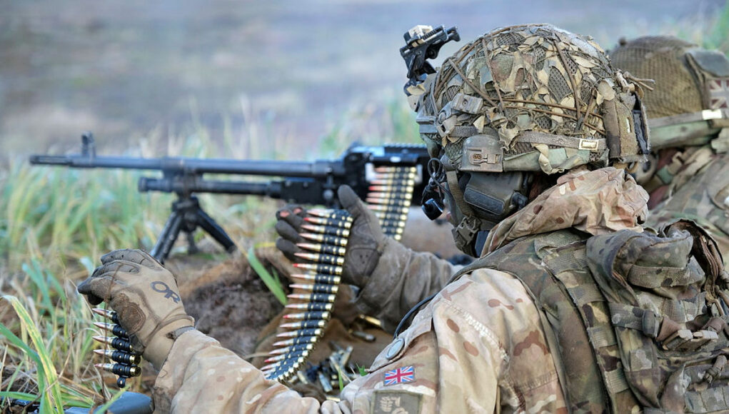 45167088.jpg.iCe34tiBMm2_FV9jYBMA.FGHHjdt3LA Soldier in desert camouflage gear and helmet feeding a belt-fed machine gun in tall grass.