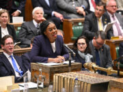 Badenoch offers support to fund warfare through welfare cuts Politician in a purple blazer speaks into a microphone at a ceremonial desk in a parliamentary chamber, with lawmakers watching.