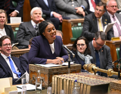 Badenoch offers support to fund warfare through welfare cuts Politician in a purple blazer speaks into a microphone at a ceremonial desk in a parliamentary chamber, with lawmakers watching.